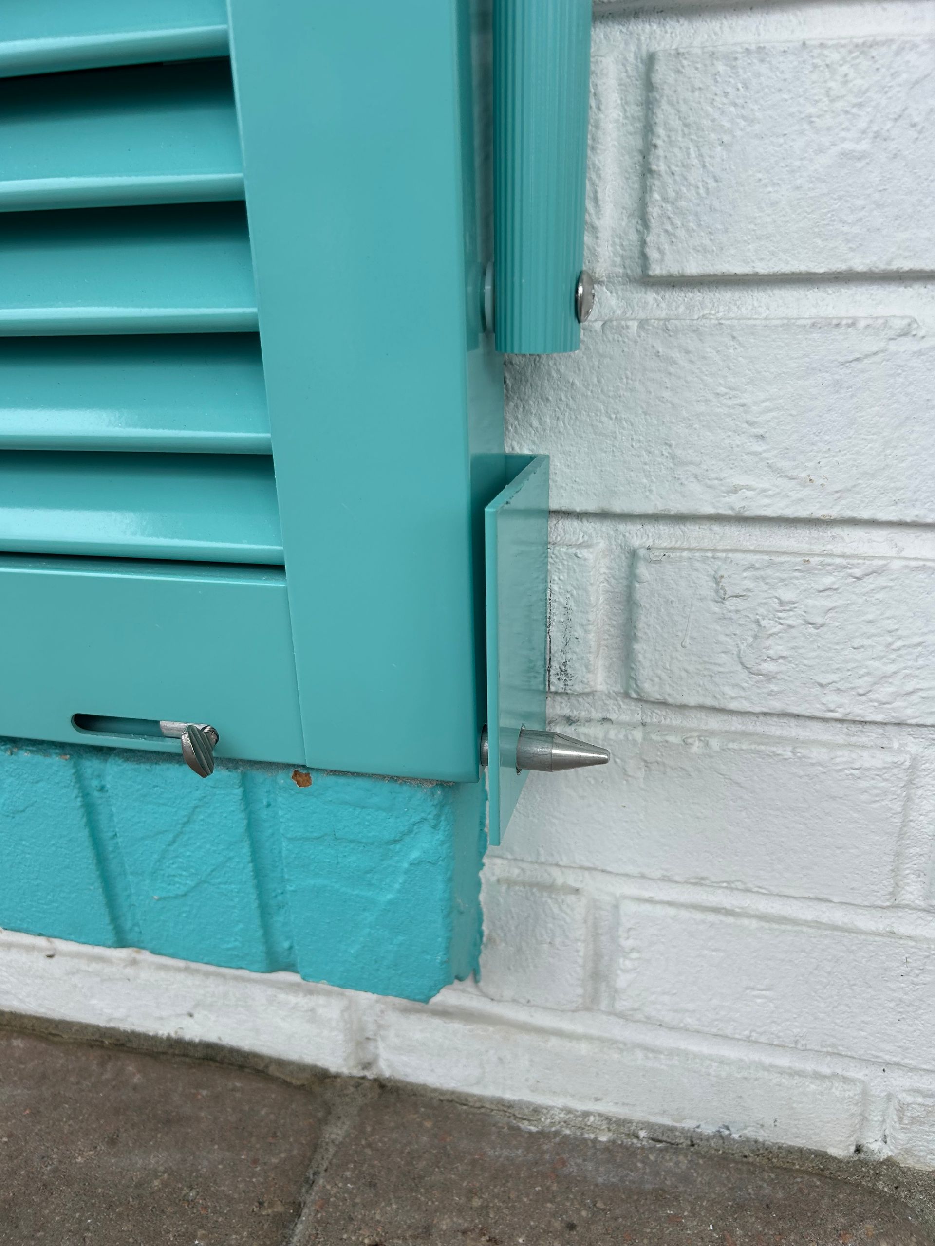 Teal shutter attached to a white brick wall by a metal bracket.