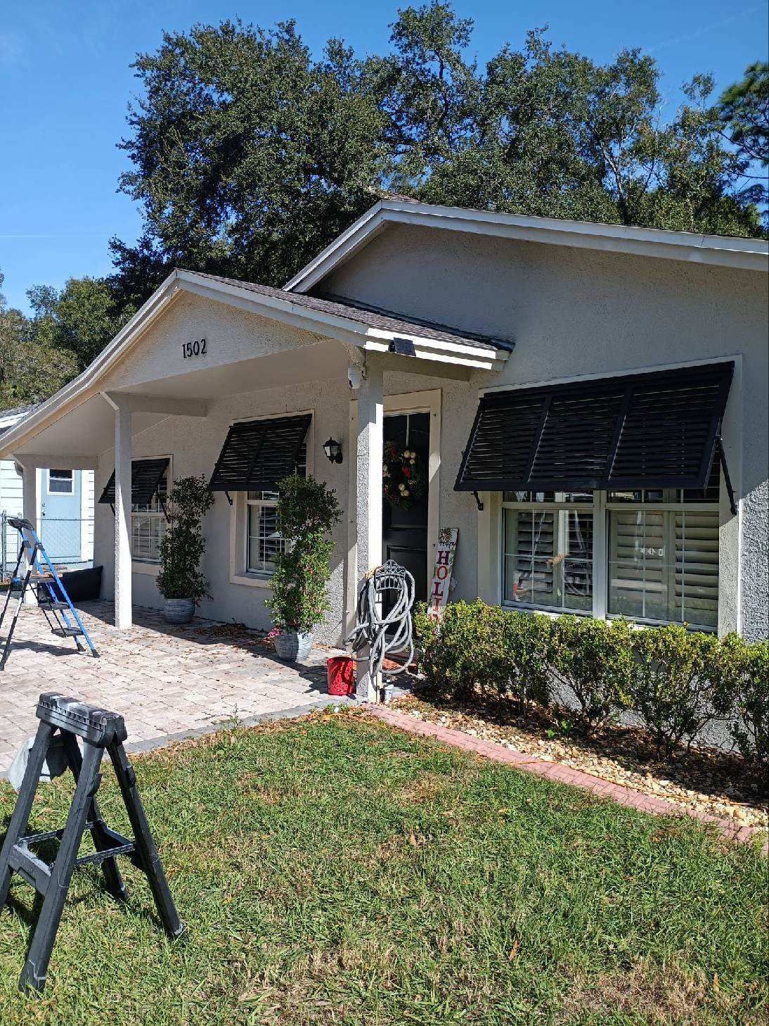 A light-colored stucco house with black awnings, front porch, and small lawn.