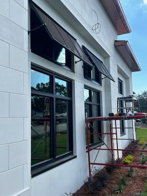 Exterior of building with black-framed windows, awnings, and white brick. A scaffolding is also visible.
