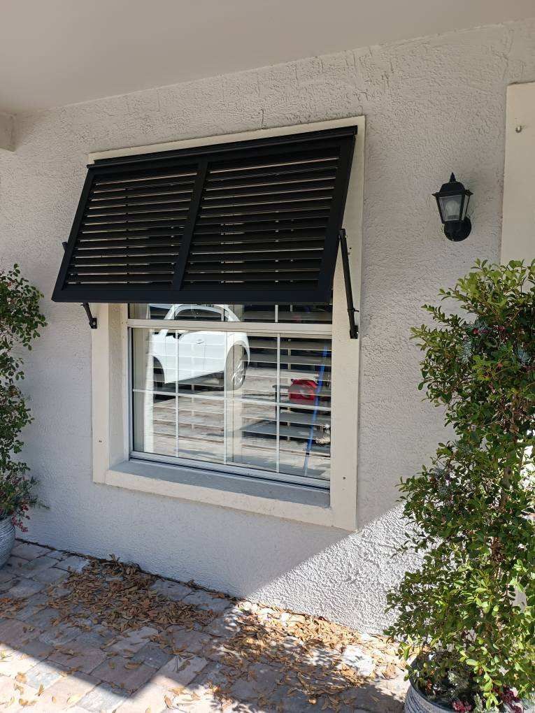 Window with black shutters open, white frame, and white car visible through glass.
