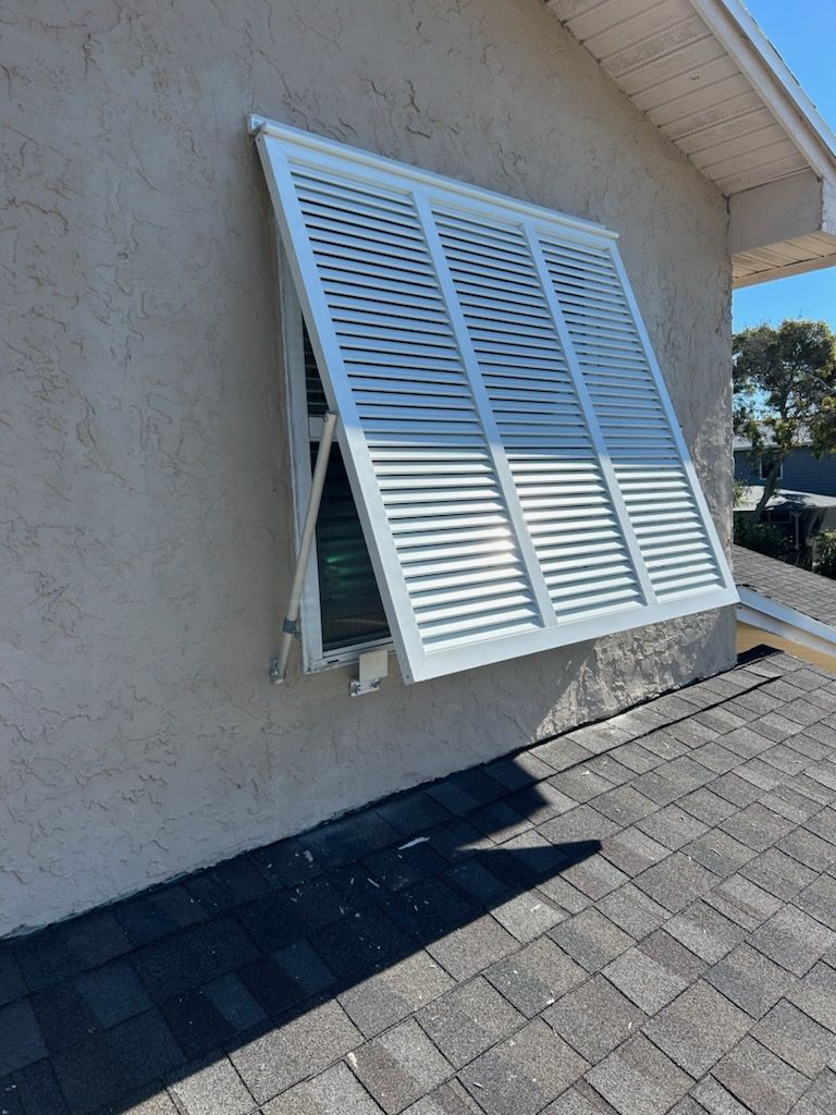 White louvered window shutter, partially open, against a stucco wall, on a rooftop.