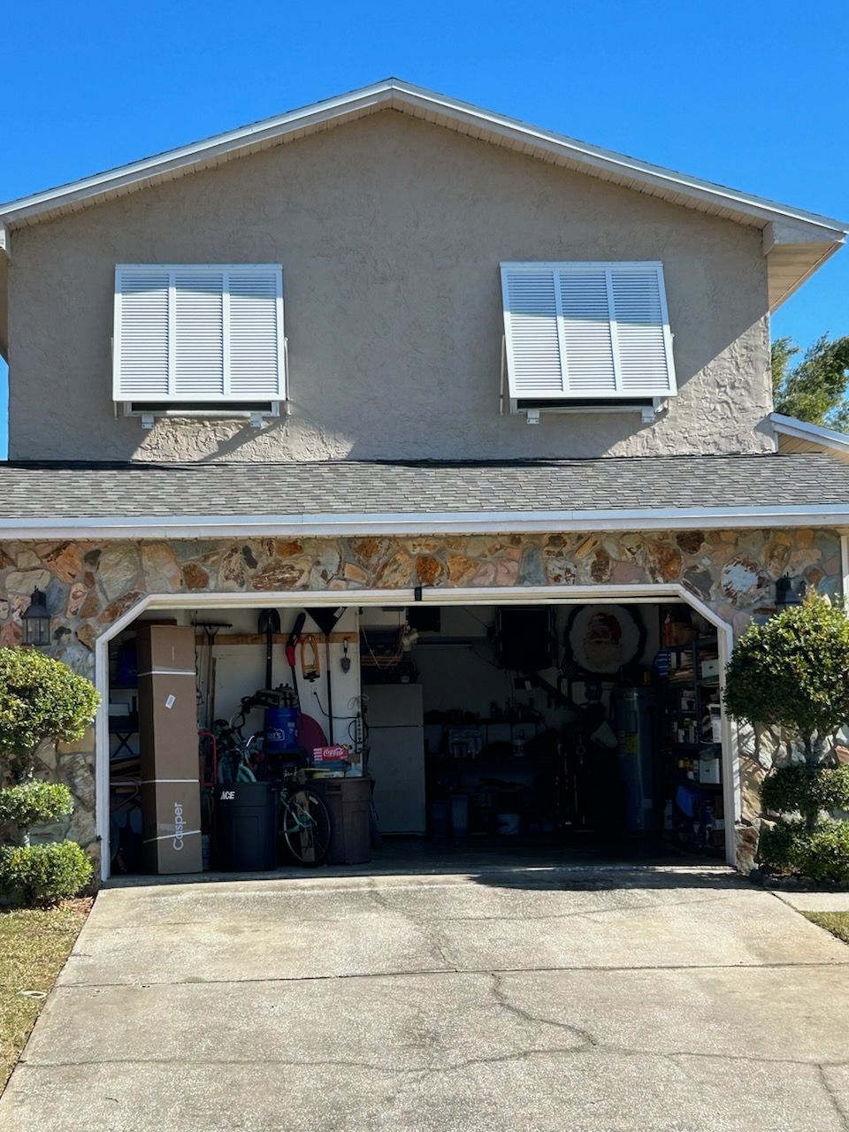 Two-story house with open garage. Upper level has two windows with white awnings, stone facade at the garage.