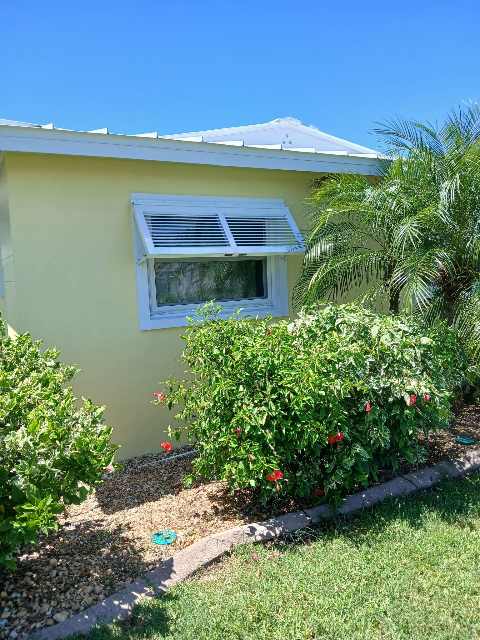 Yellow building with awning window, surrounded by green bushes, blue sky overhead.