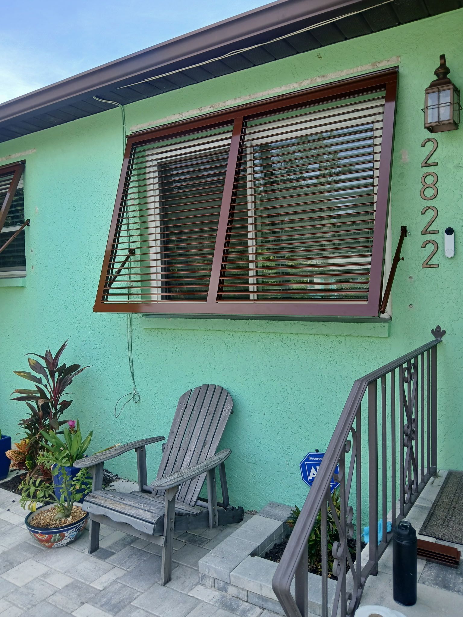 Green stucco house with wooden shutters, a chair, and steps.
