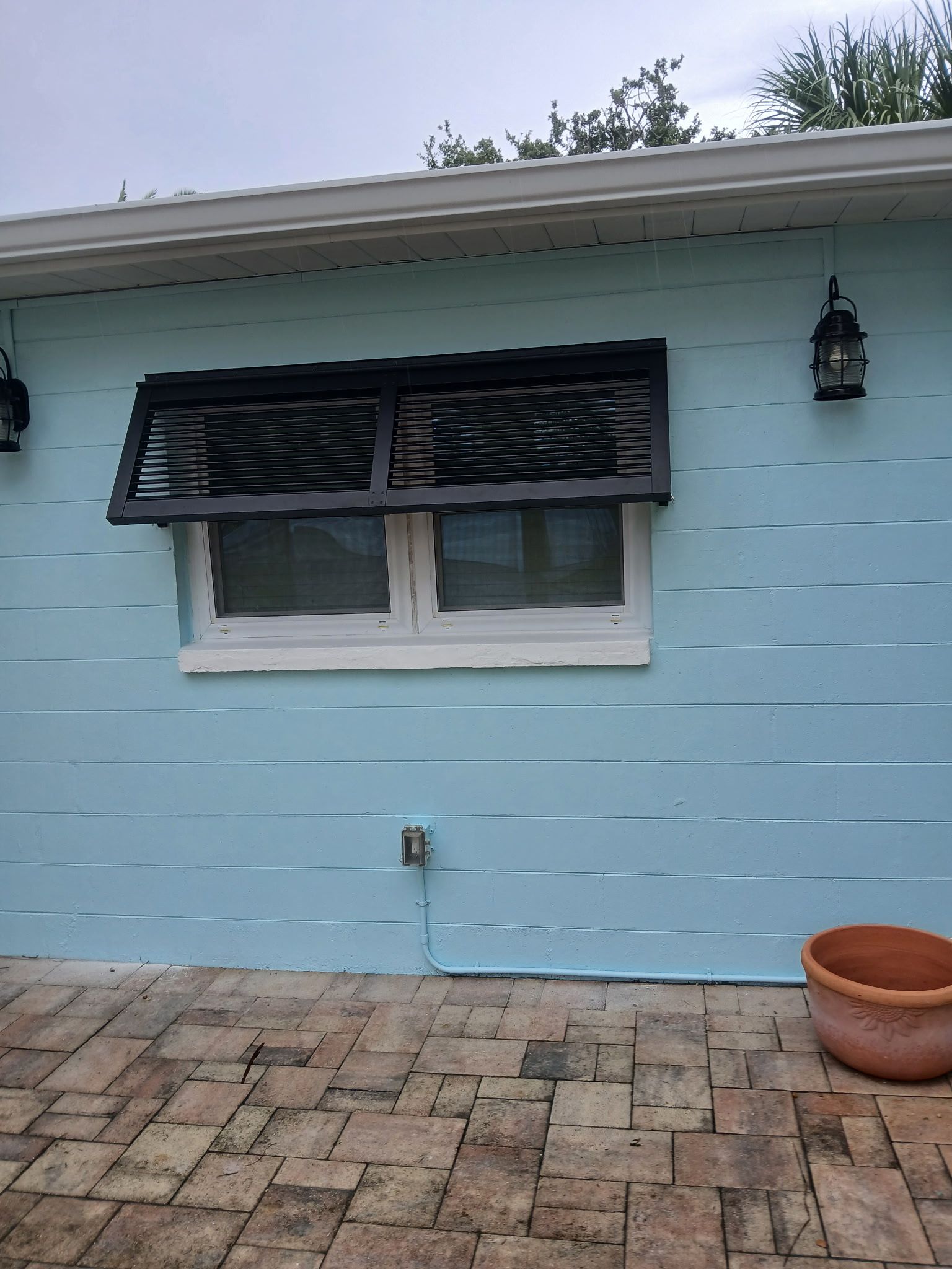 Blue building with a window and black shutter, two lanterns, and a brick patio.