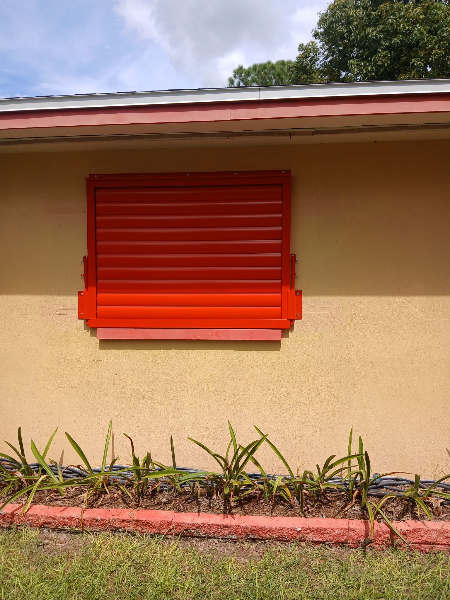 Red storm shutter over a window on a tan stucco wall.