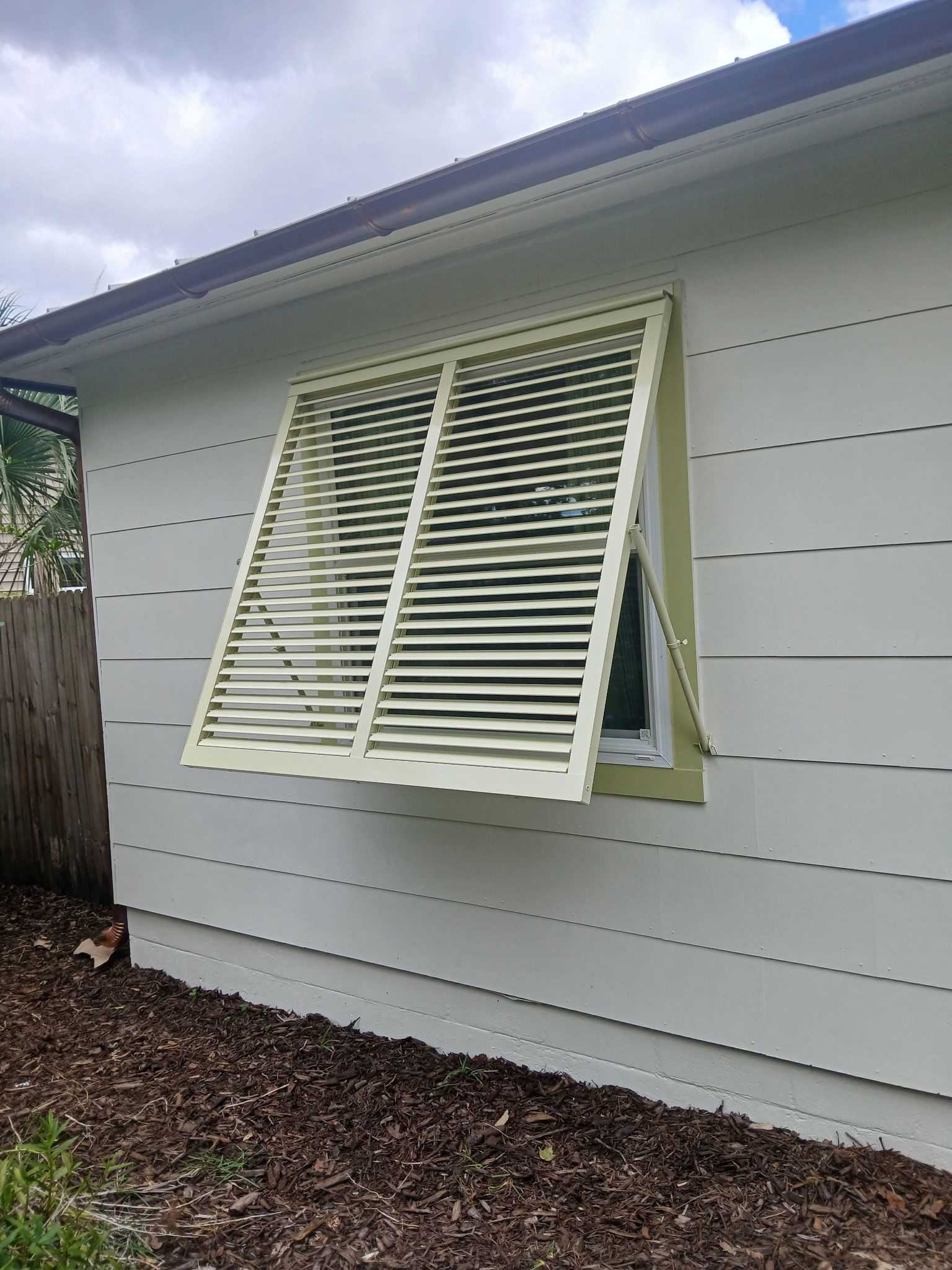 Beige shutter open over a window on a white house.