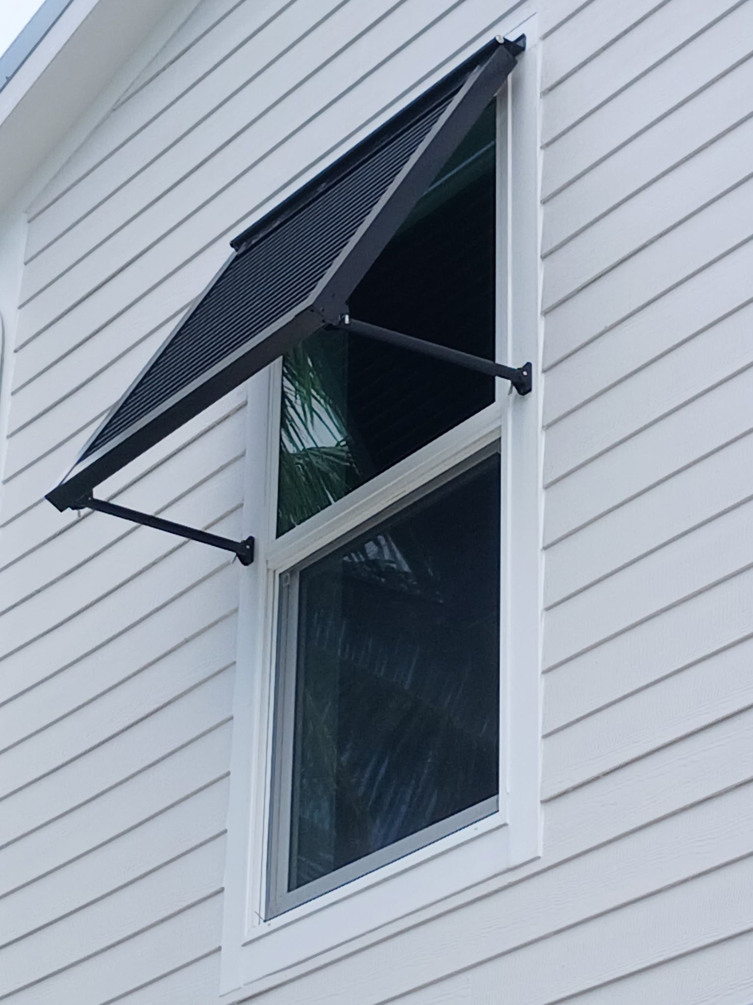 Black awning over a white window on a white clapboard house.