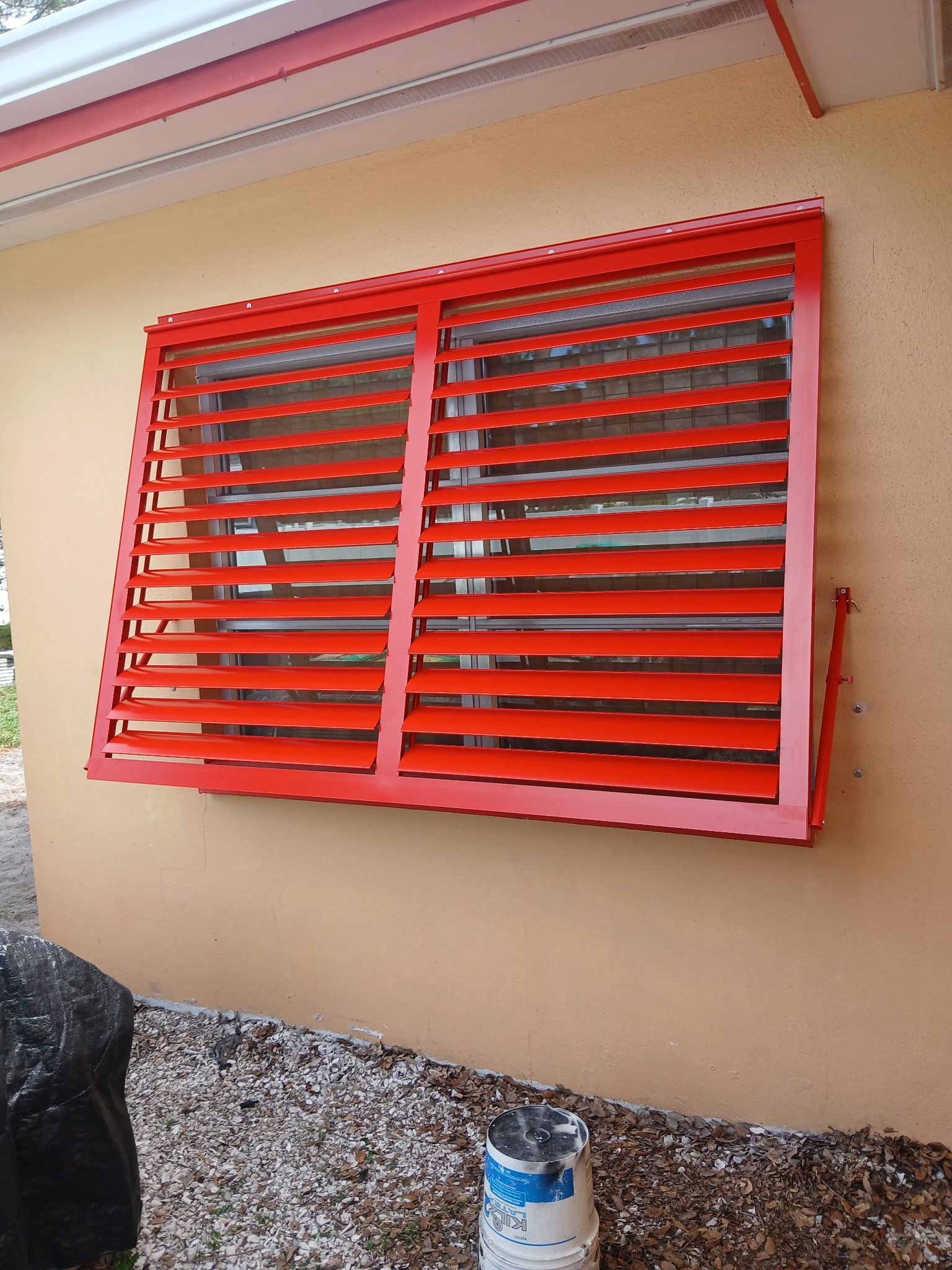 Red slatted window covering a window on a tan building.