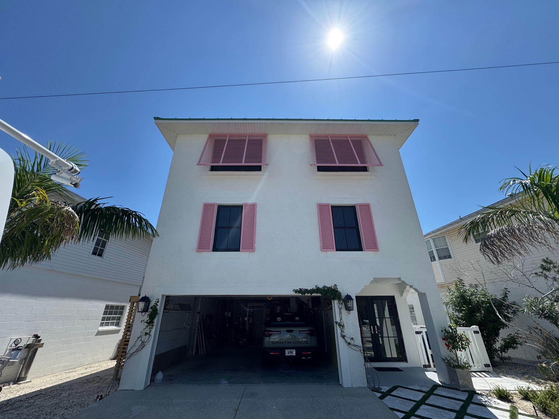 White house with pink shutters, open garage, blue sky, and bright sun.