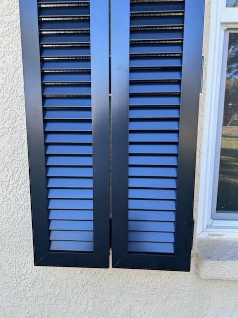 Black louvered shutters on a stucco wall beside a white-framed window.