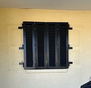 Black closed shutters on a yellow stucco wall, viewed from the outside.