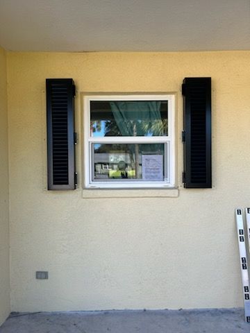 Exterior view of a window with black shutters on a pale yellow wall.