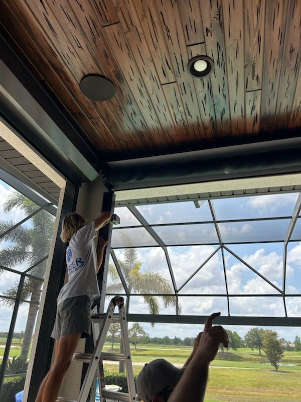 Person on a ladder installing a roll-down screen on a screened porch with a view of a golf course.