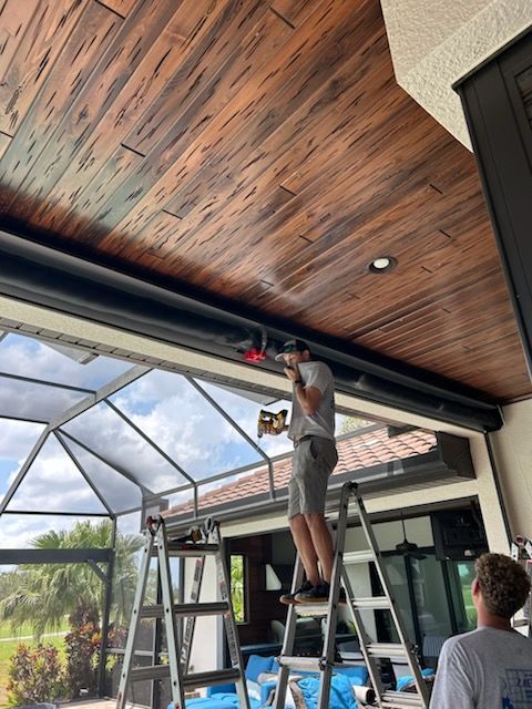 Two men installing a retractable awning on a patio with a wood-look ceiling. One man is on a ladder.