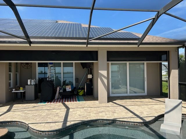 Backyard with pool, patio, and house with solar panels. Black rolling shutters are down over some windows.