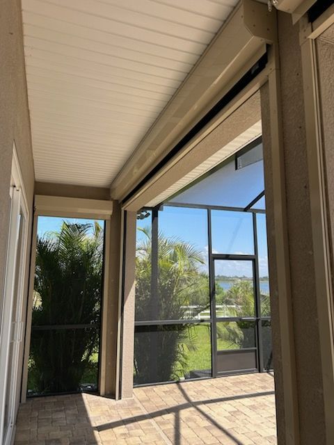 Screened porch with retractable sun shade, light brown frame and ceiling, views of trees and water.