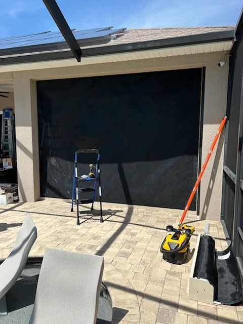Black screen installed on a patio, blue ladder, tools, beige pavers, sunny outdoor setting.