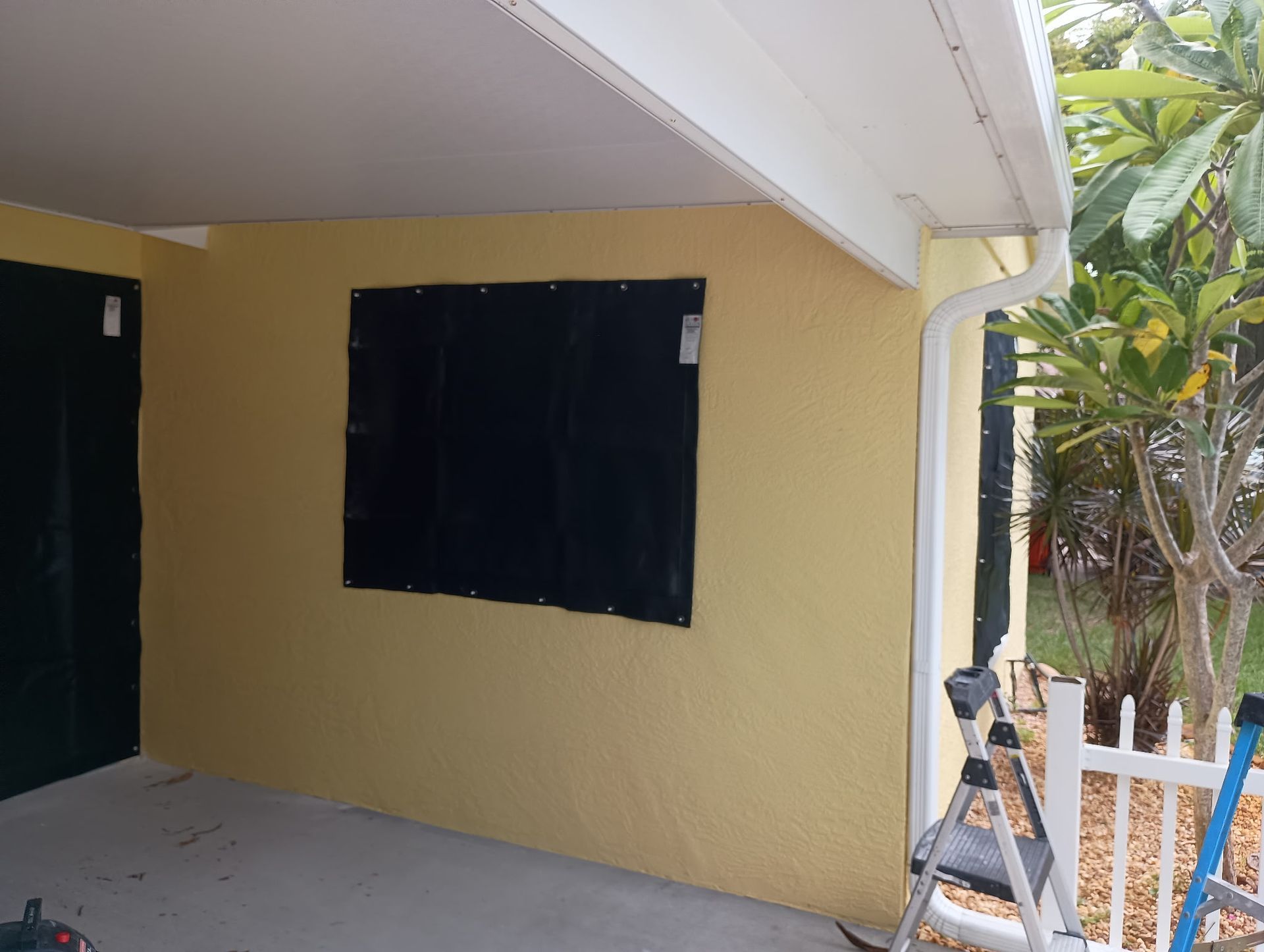 Yellow building exterior with a covered window, next to a white gutter and fence.