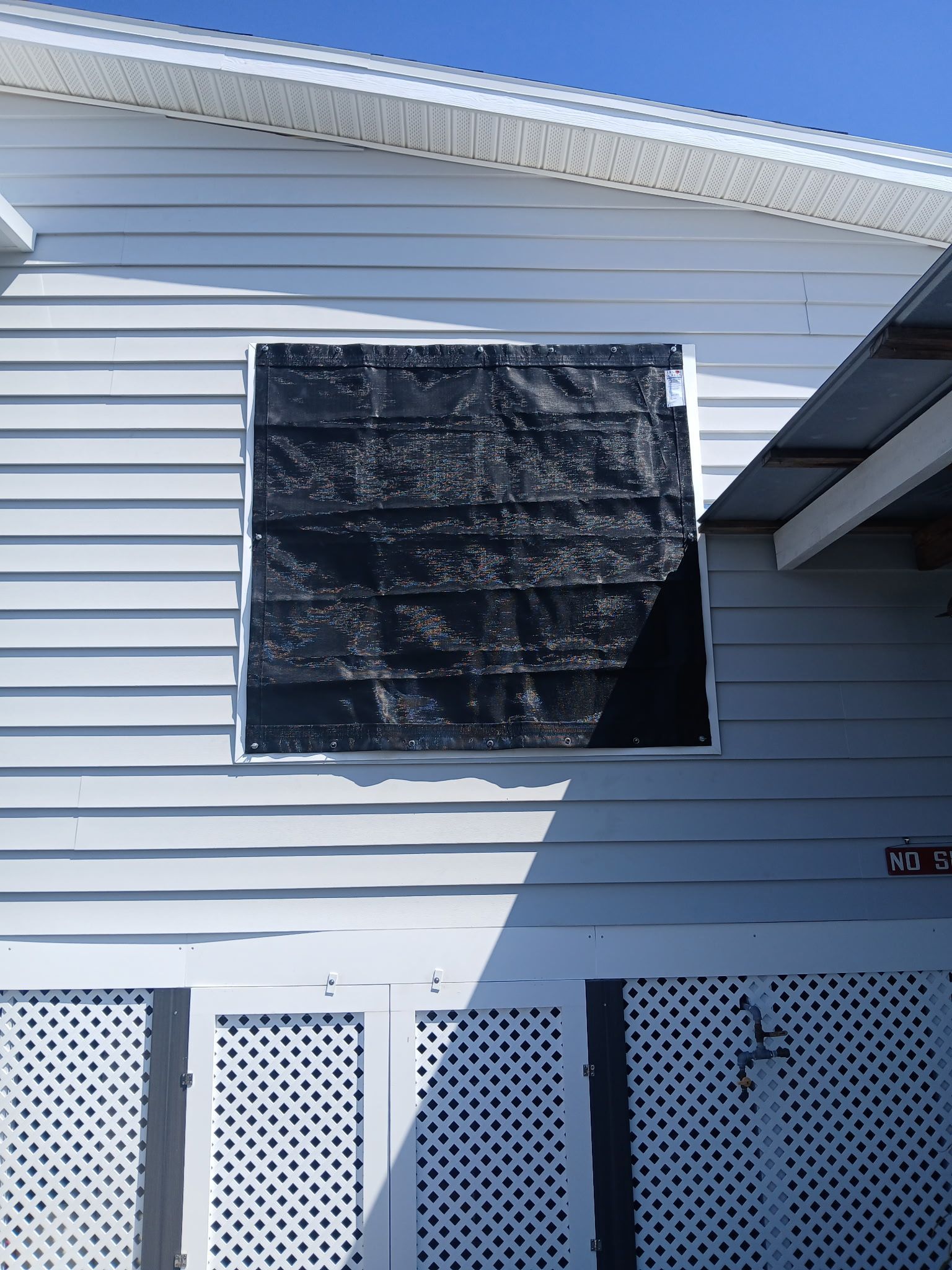 Exterior of a white house with a window covered by a black tarp.