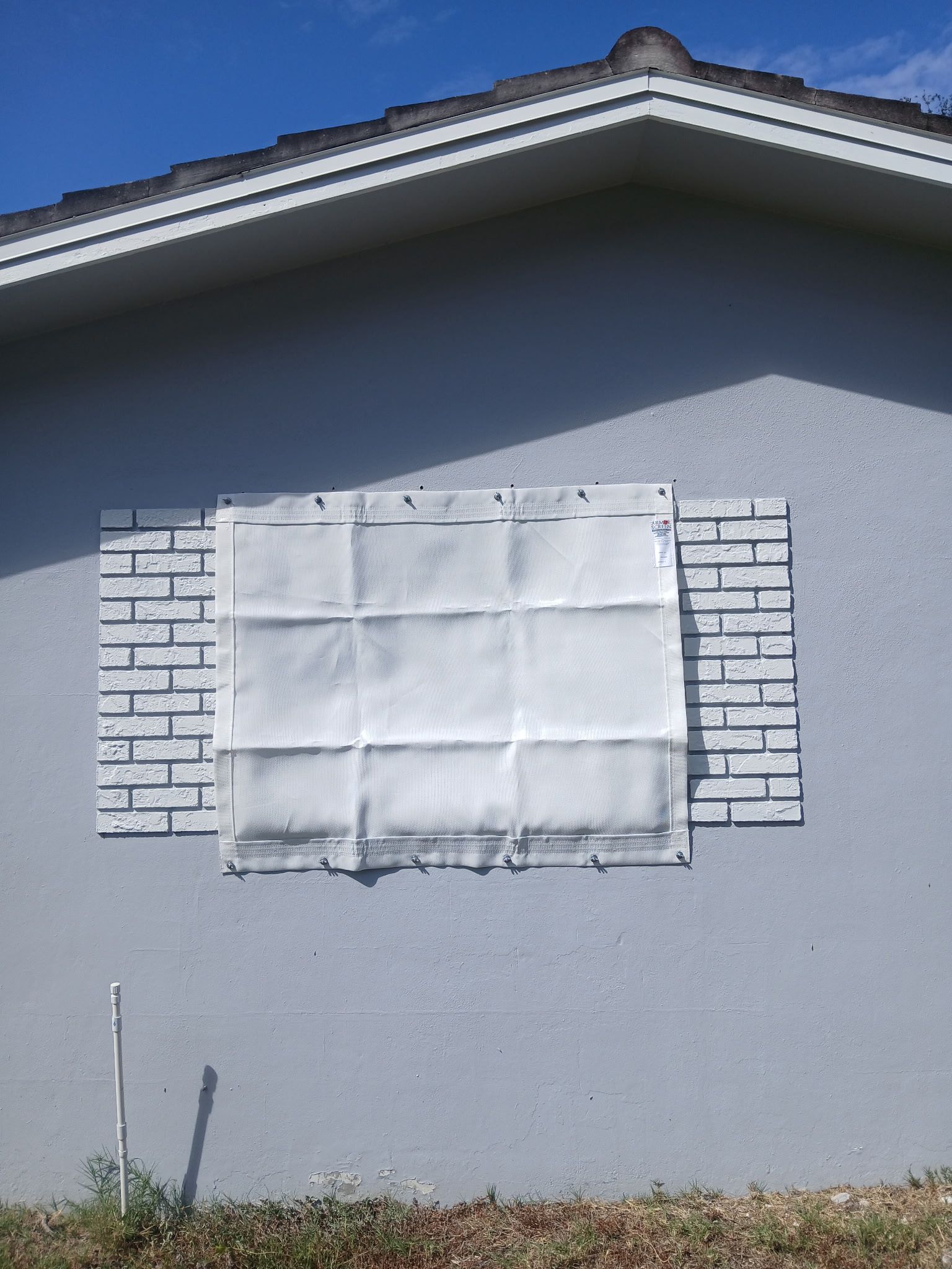 Exterior house wall with boarded-up window, brick accents, and blue sky.