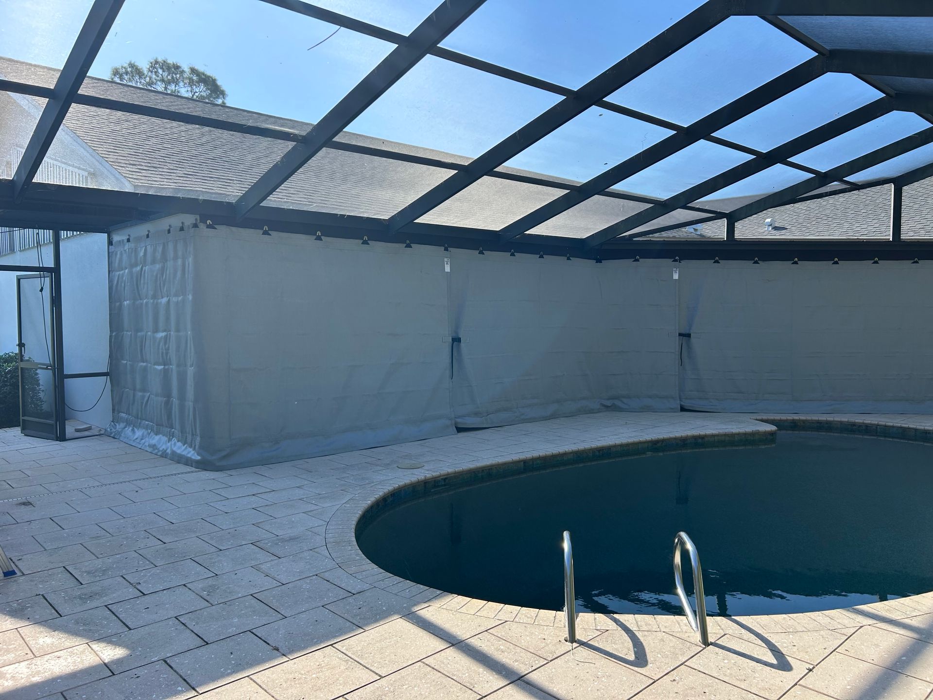 Pool enclosure with retractable gray curtains, pool, and brick patio under a clear roof.