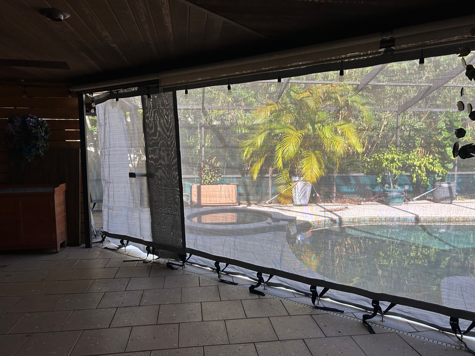 Patio with retractable screen overlooking a pool and trees. Dark screen and frame with a partially visible pool.