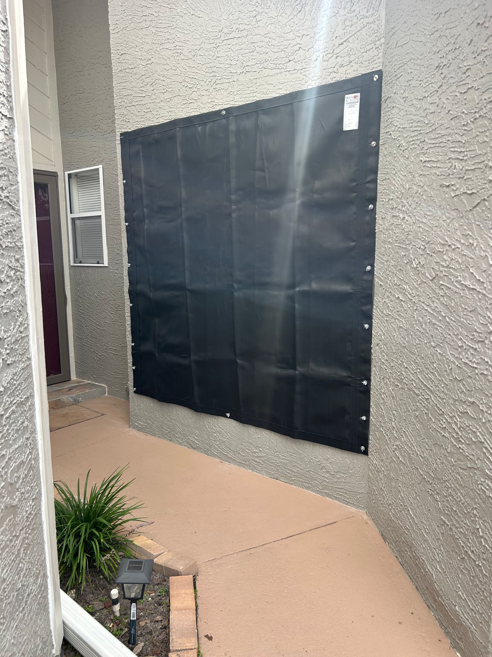 Black tarp covers a wall. Pathway and small plant are in front. Building exterior.
