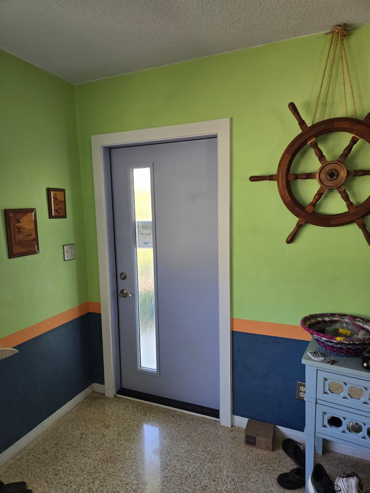 Interior doorway with light blue door and white trim, lime green walls with blue and orange accent, and a ship's wheel.