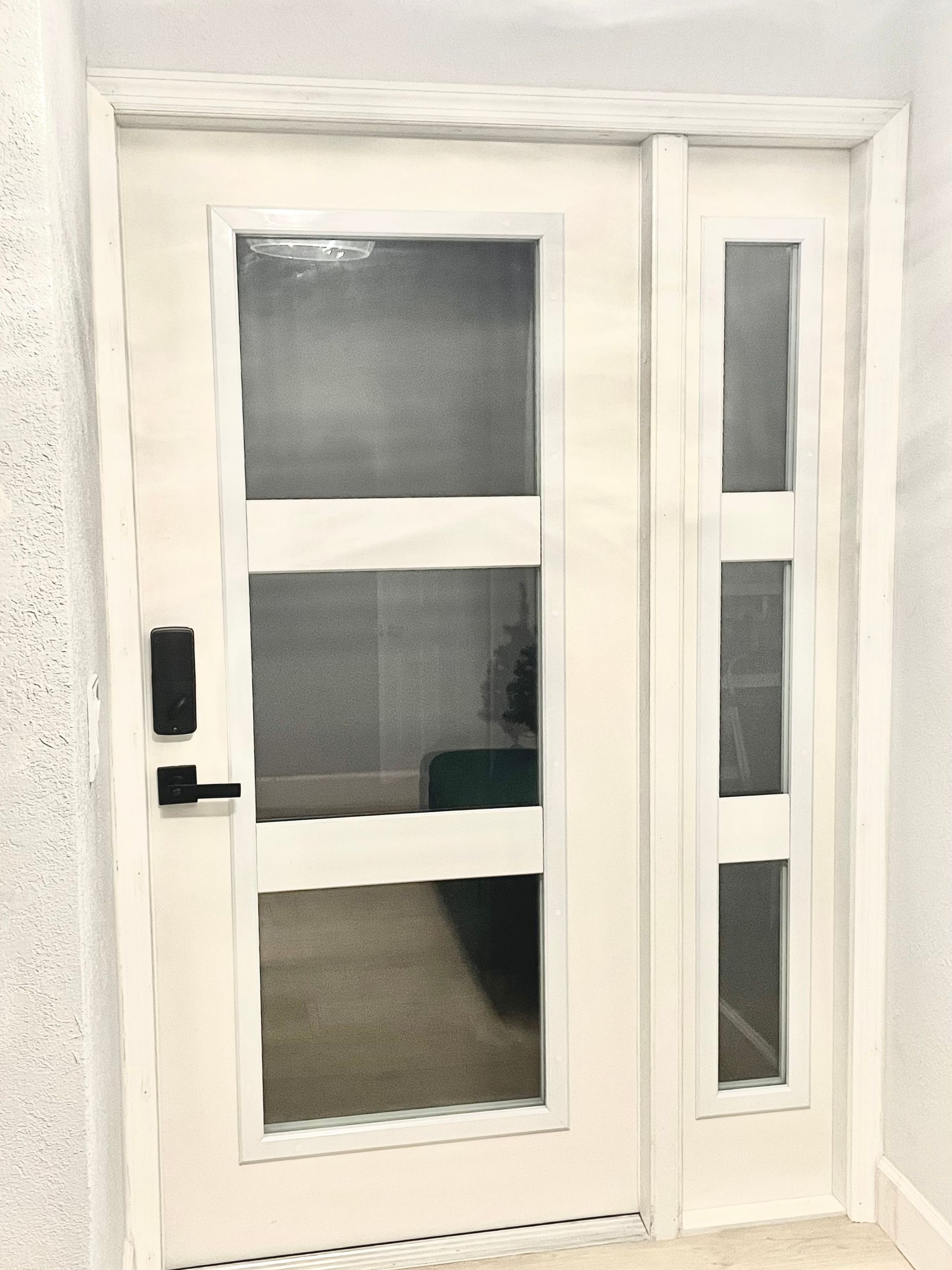 White door with glass panels and sidelight, black door handle.