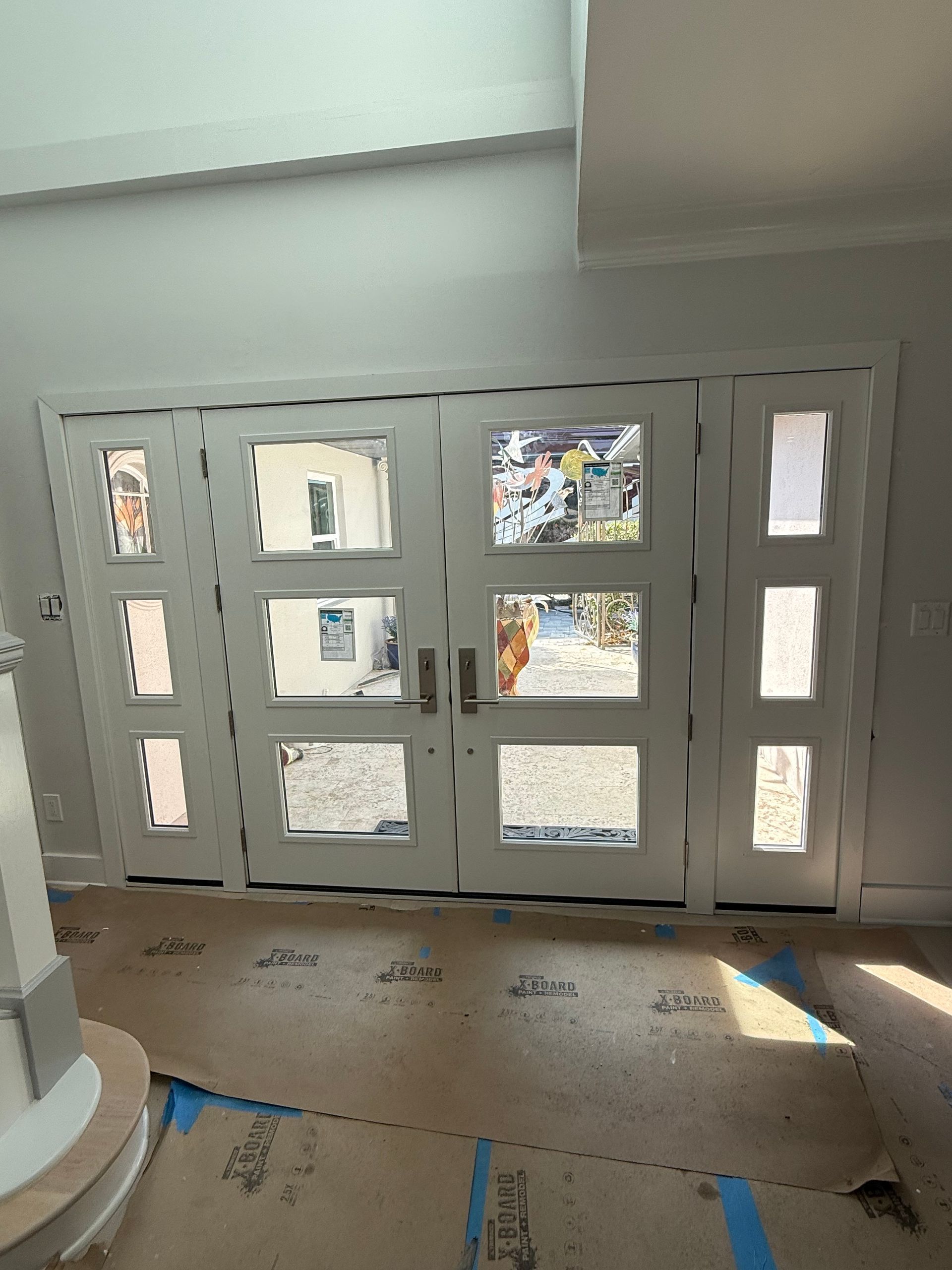 White French doors with multiple glass panels, in a light-filled interior. Blue tape on the floor.