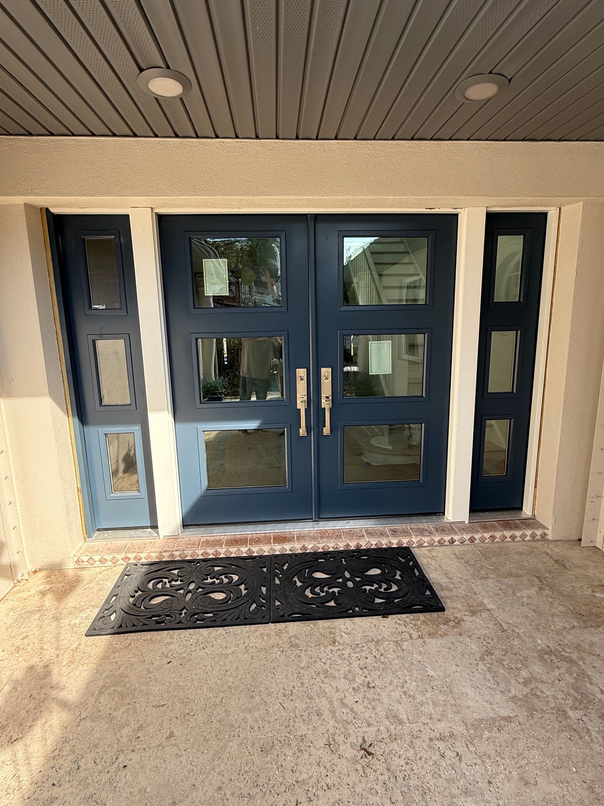Blue double doors with glass panels; black doormat; exterior of a building.