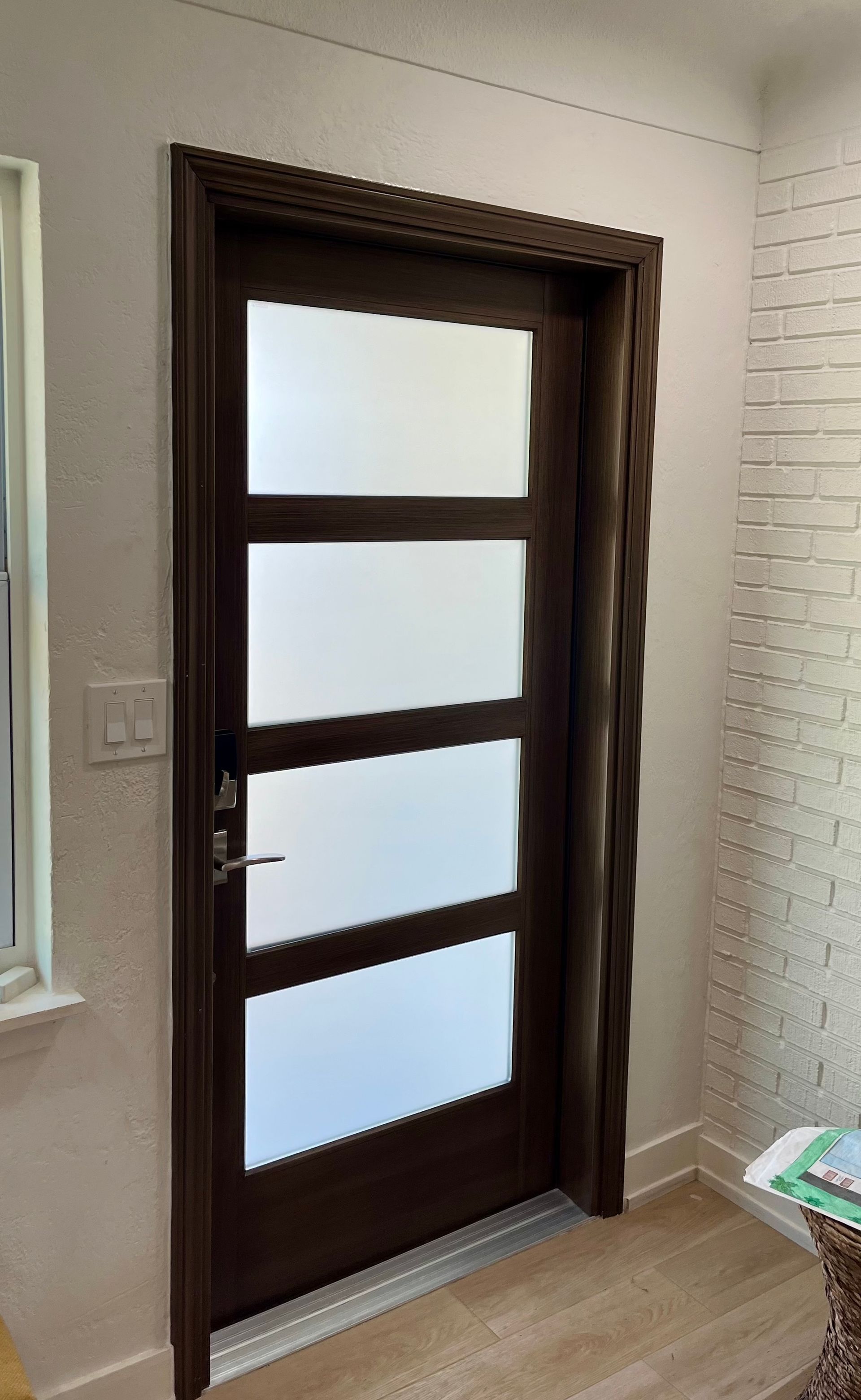 Brown door with four frosted glass panels, surrounded by dark wood trim. White walls and wood flooring.