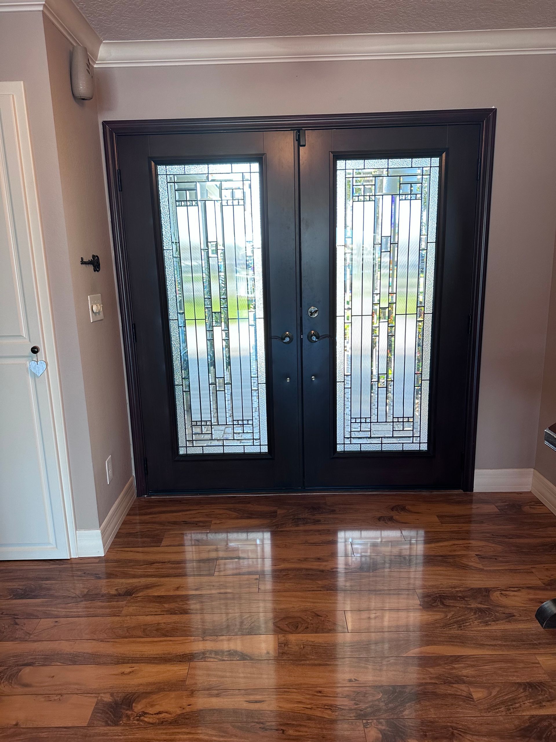 Double black doors with textured glass panels, set in a wood-look frame, on a glossy hardwood floor.