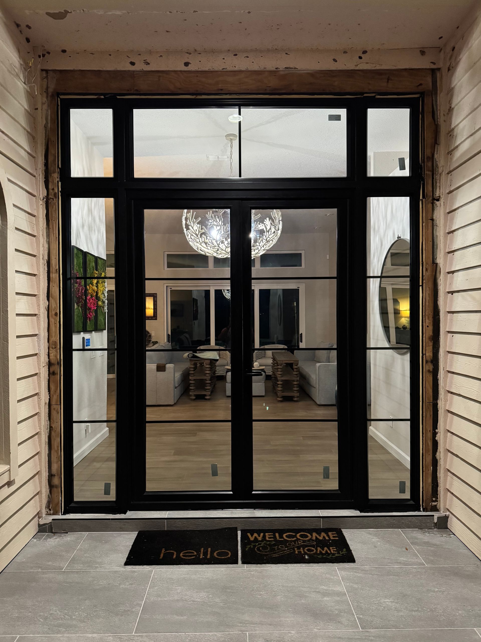 Black framed double doors with sidelights; neutral entryway, welcome mats.