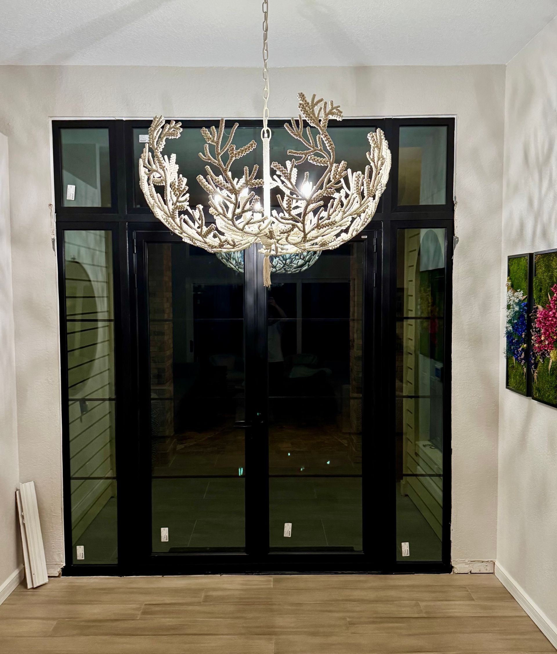 Elegant chandelier hangs above black-framed glass doors, reflected interior.
