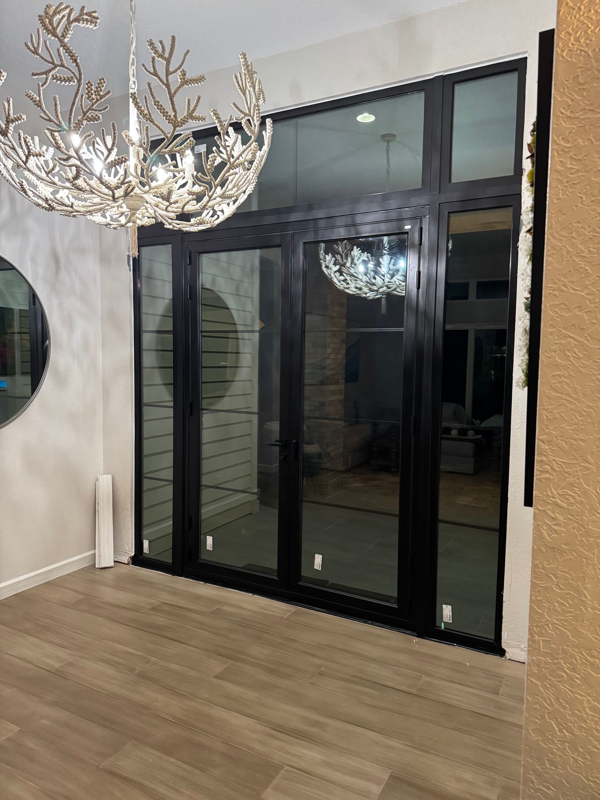 Glass doors with black frames in a brightly lit room, featuring a chandelier and light-colored flooring.