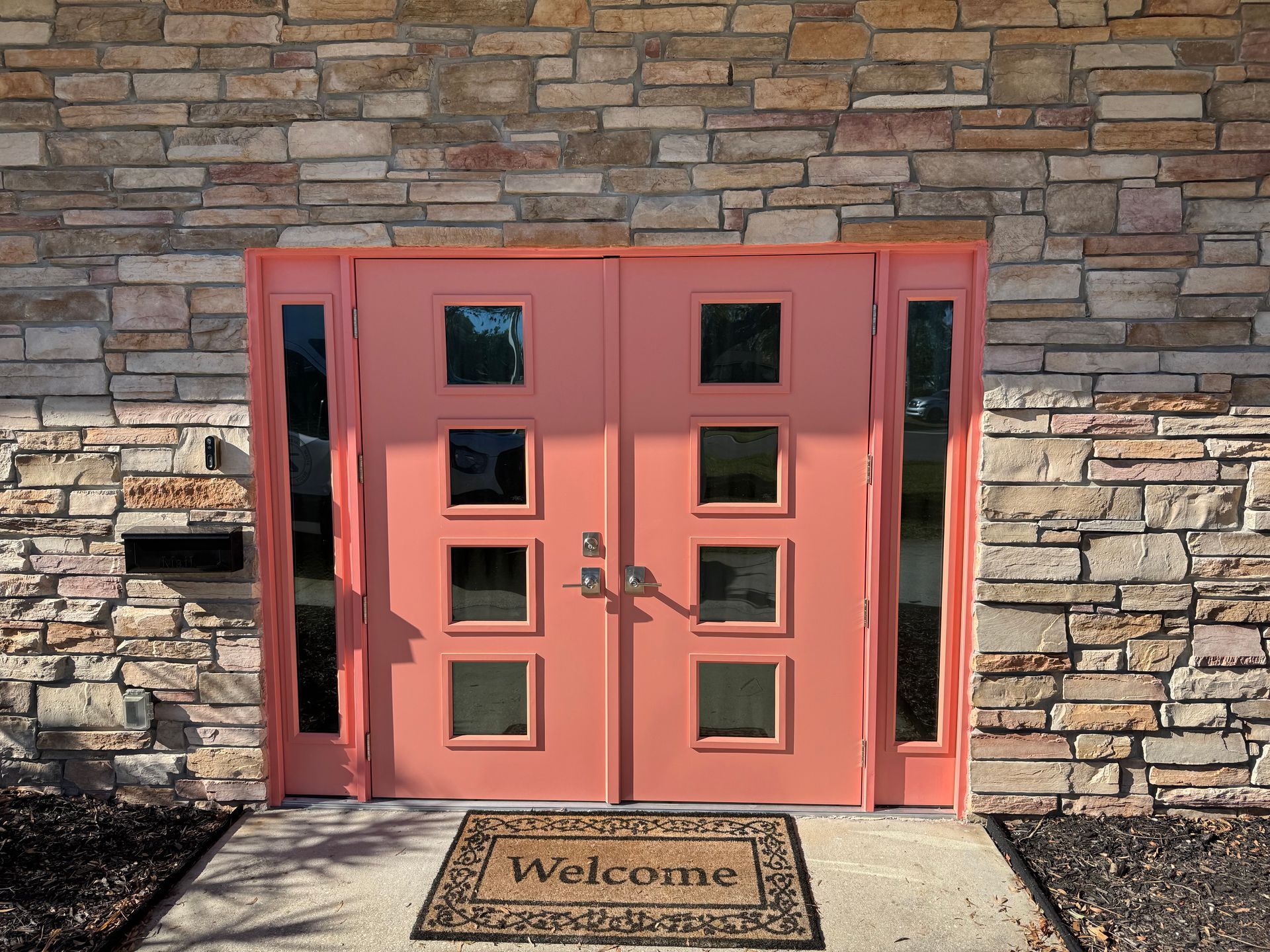 Coral pink double doors with square windows against a stone facade.