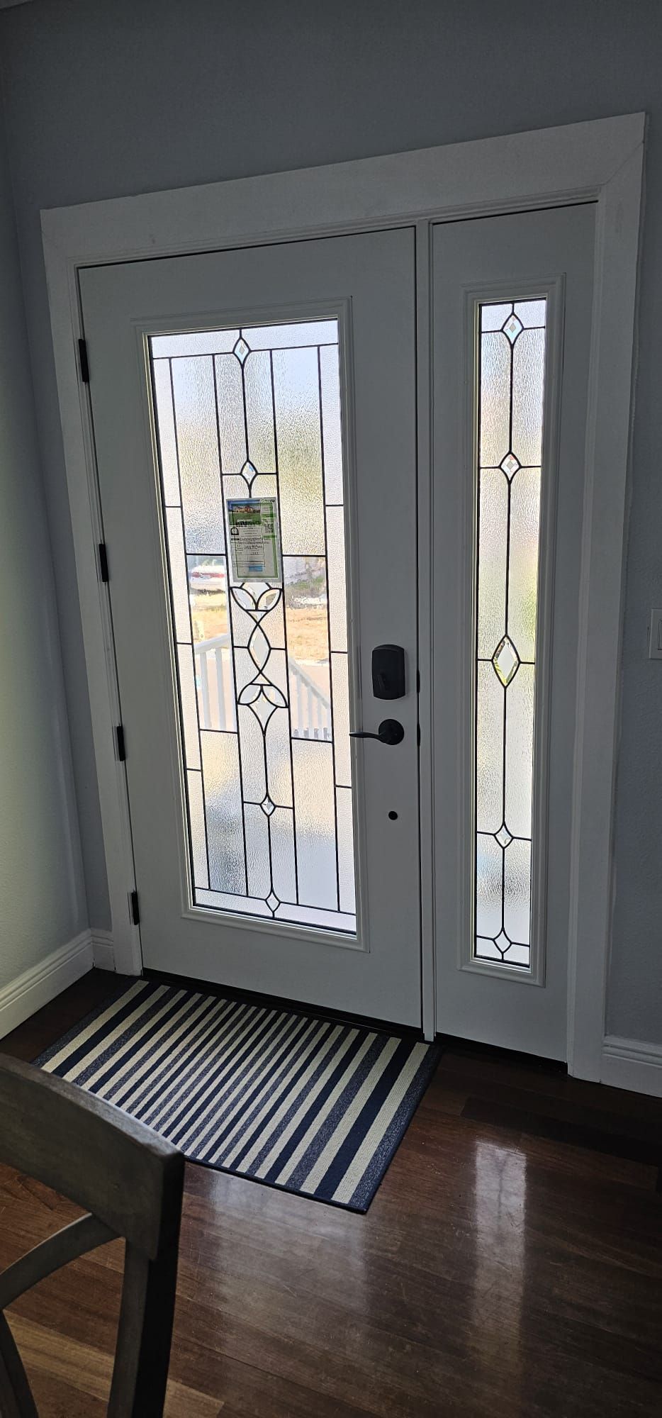 White double door with glass panes, black doormat, wooden floor.