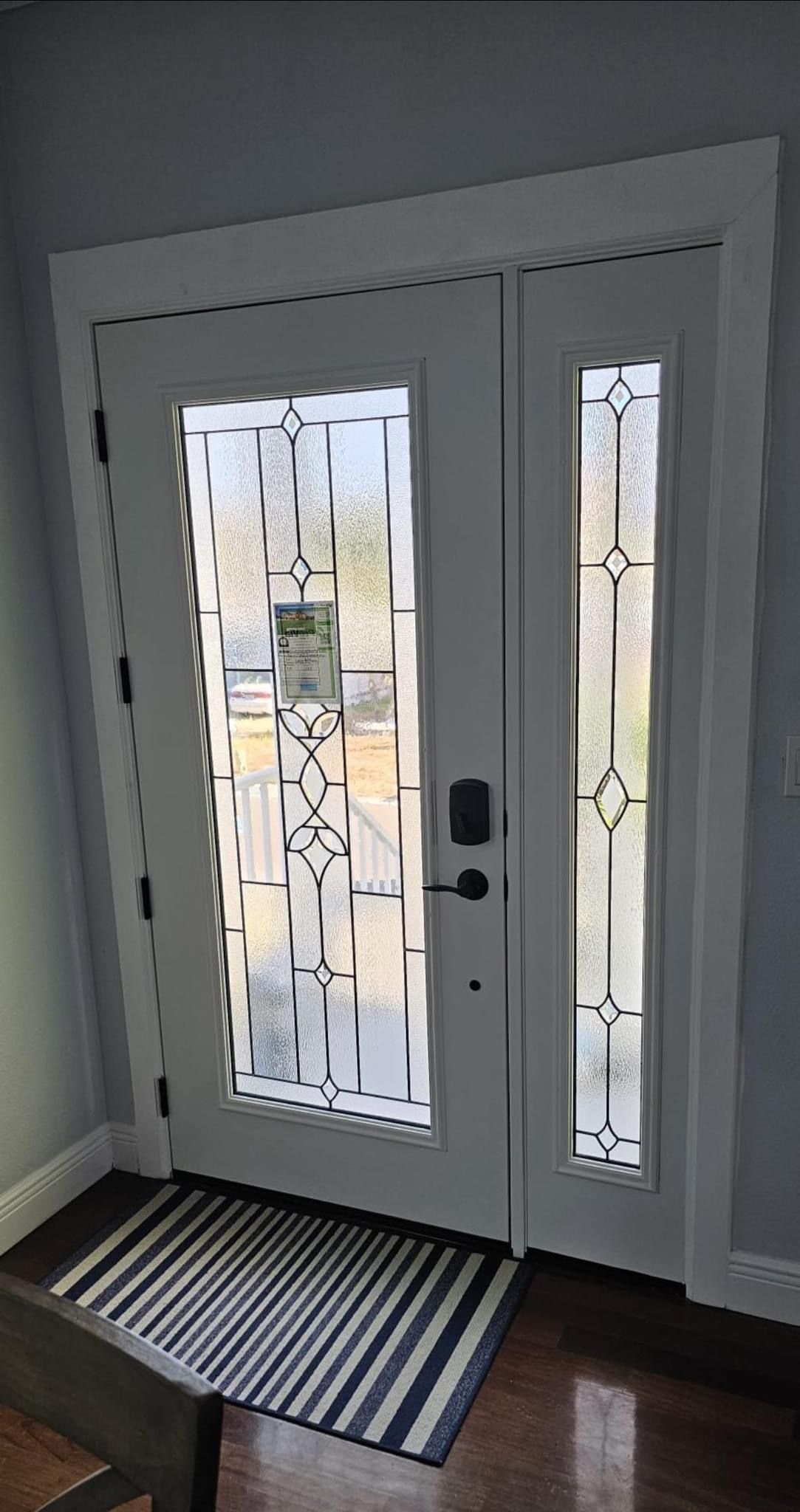 White glass-paneled double doors with black hardware and decorative trim. A striped doormat sits inside.