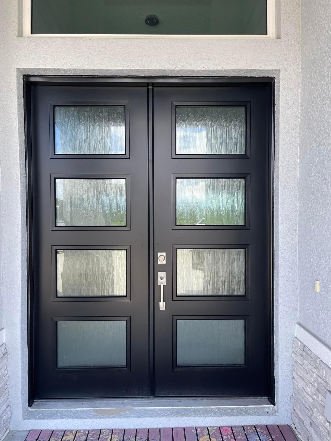 Black double doors with rectangular glass panels. Gray stucco exterior.