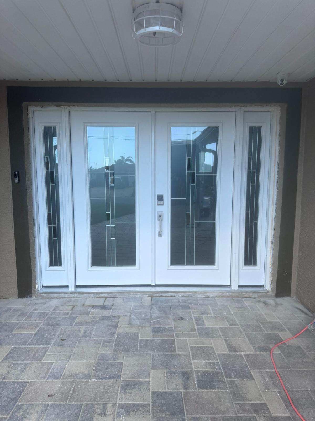 White double doors with glass panels and sidelights on a brick patio under a covered porch.