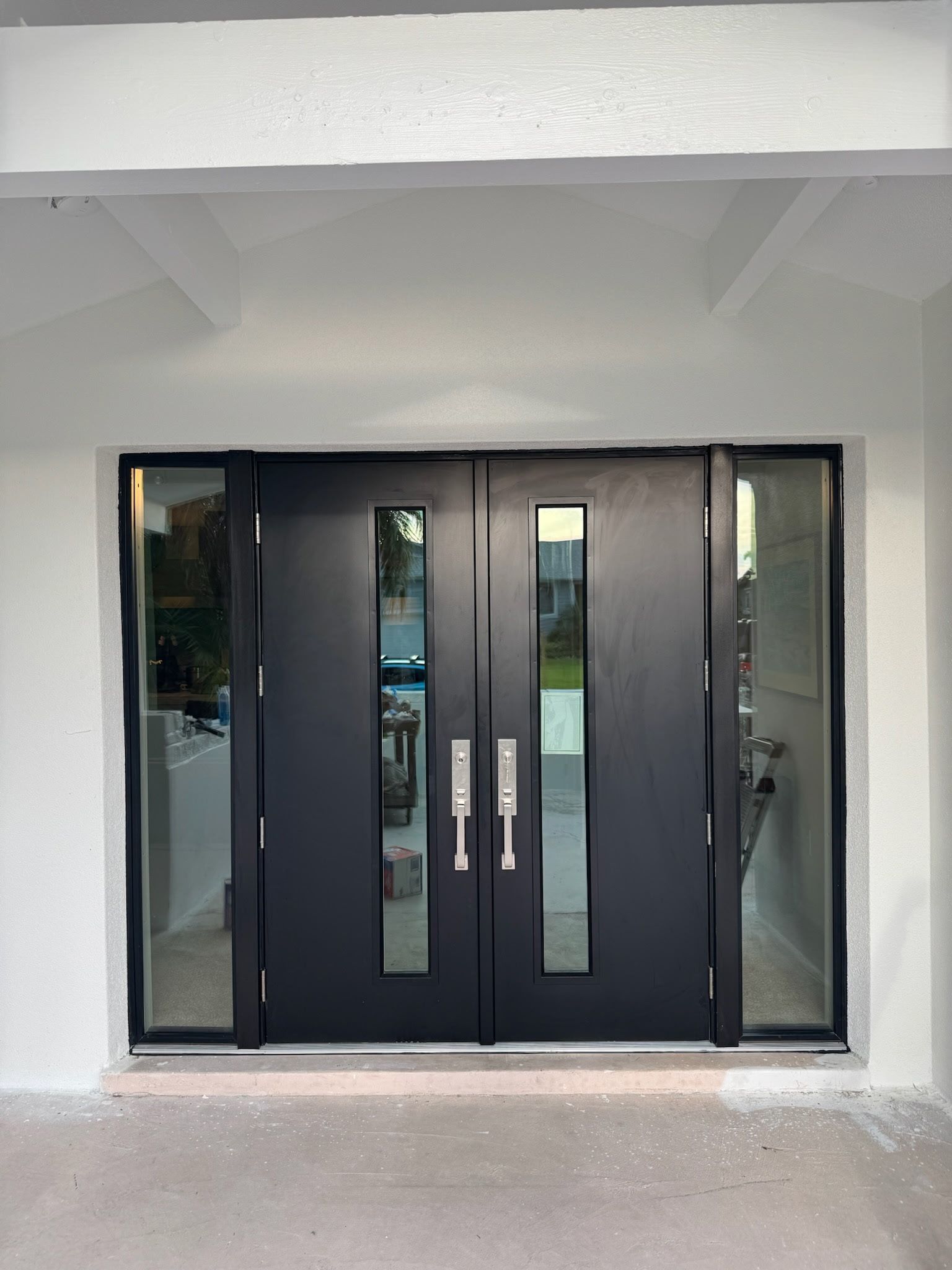 Black double front doors with glass panels and sidelights in a white frame.