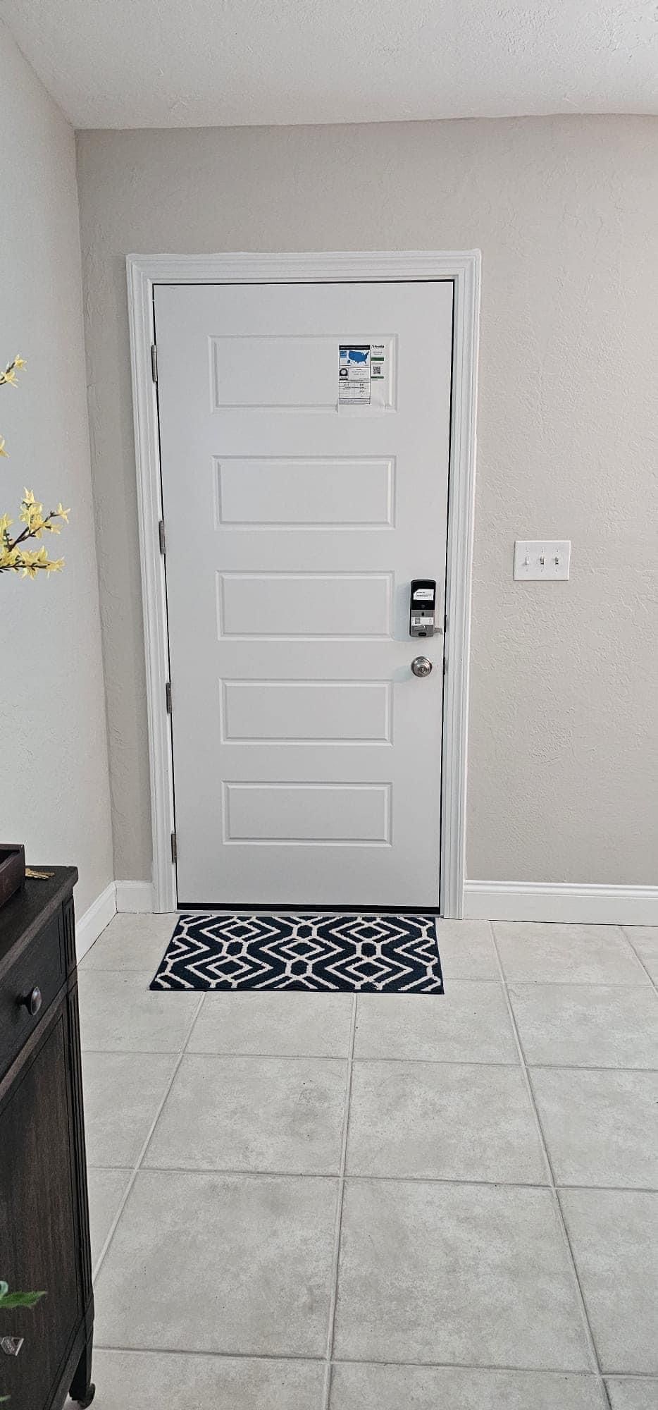 White door with black and white mat, gray tile floor, and a black dresser.
