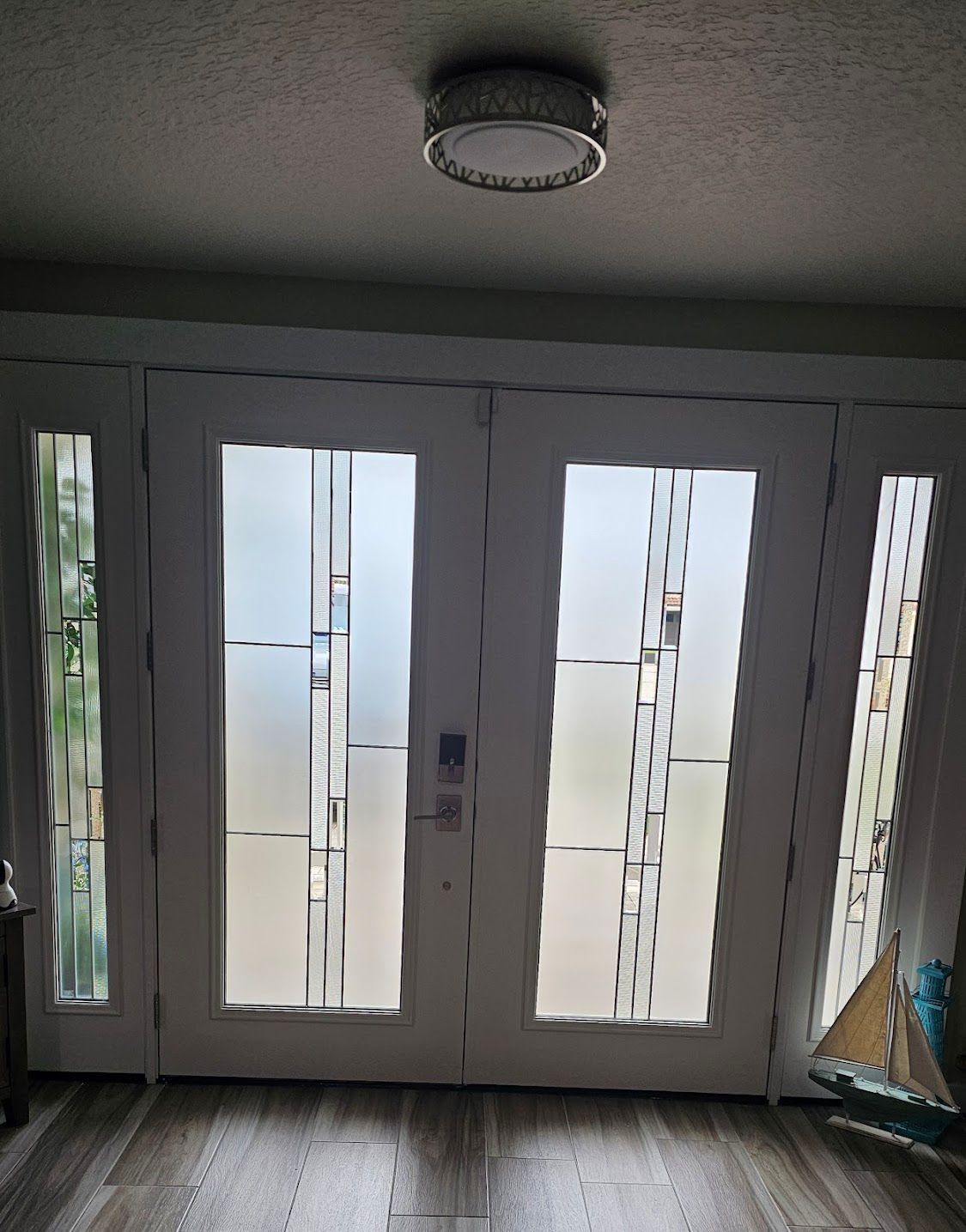 White double doors with frosted glass panels, flanked by sidelights. A round light fixture is mounted above.