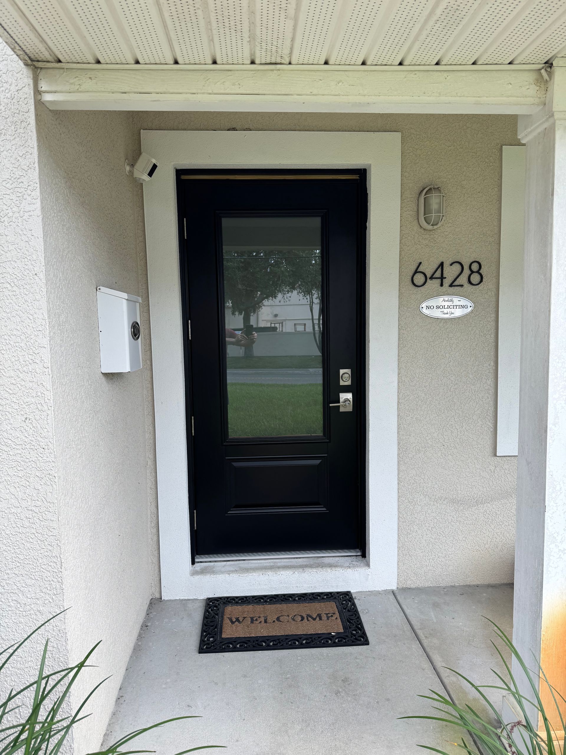 Black front door with glass panel, white trim, welcome mat, house number 6428, and a mailbox.