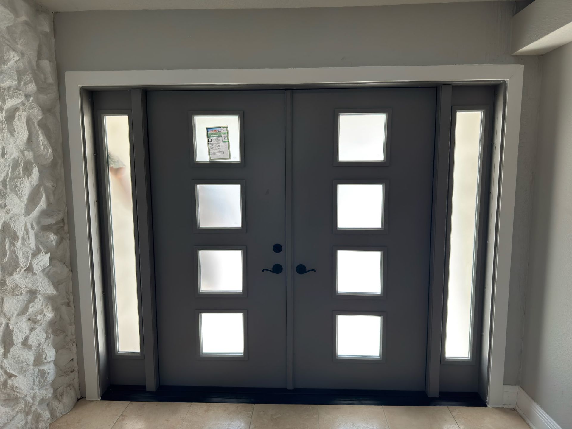 Gray double doors with frosted glass squares and sidelights. White trim surrounds the doors.