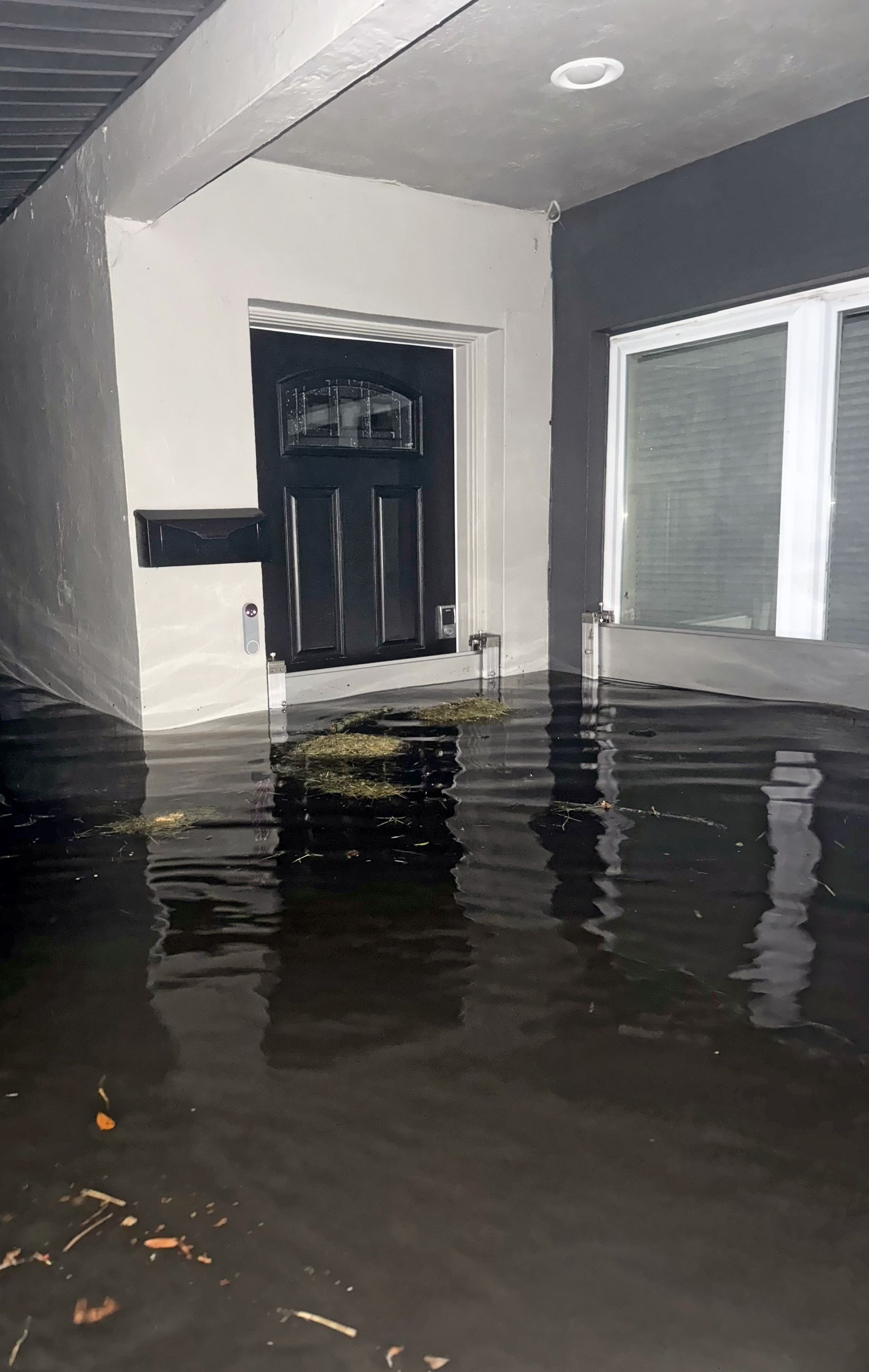 Interior room flooded with water; black door and white window frames visible.