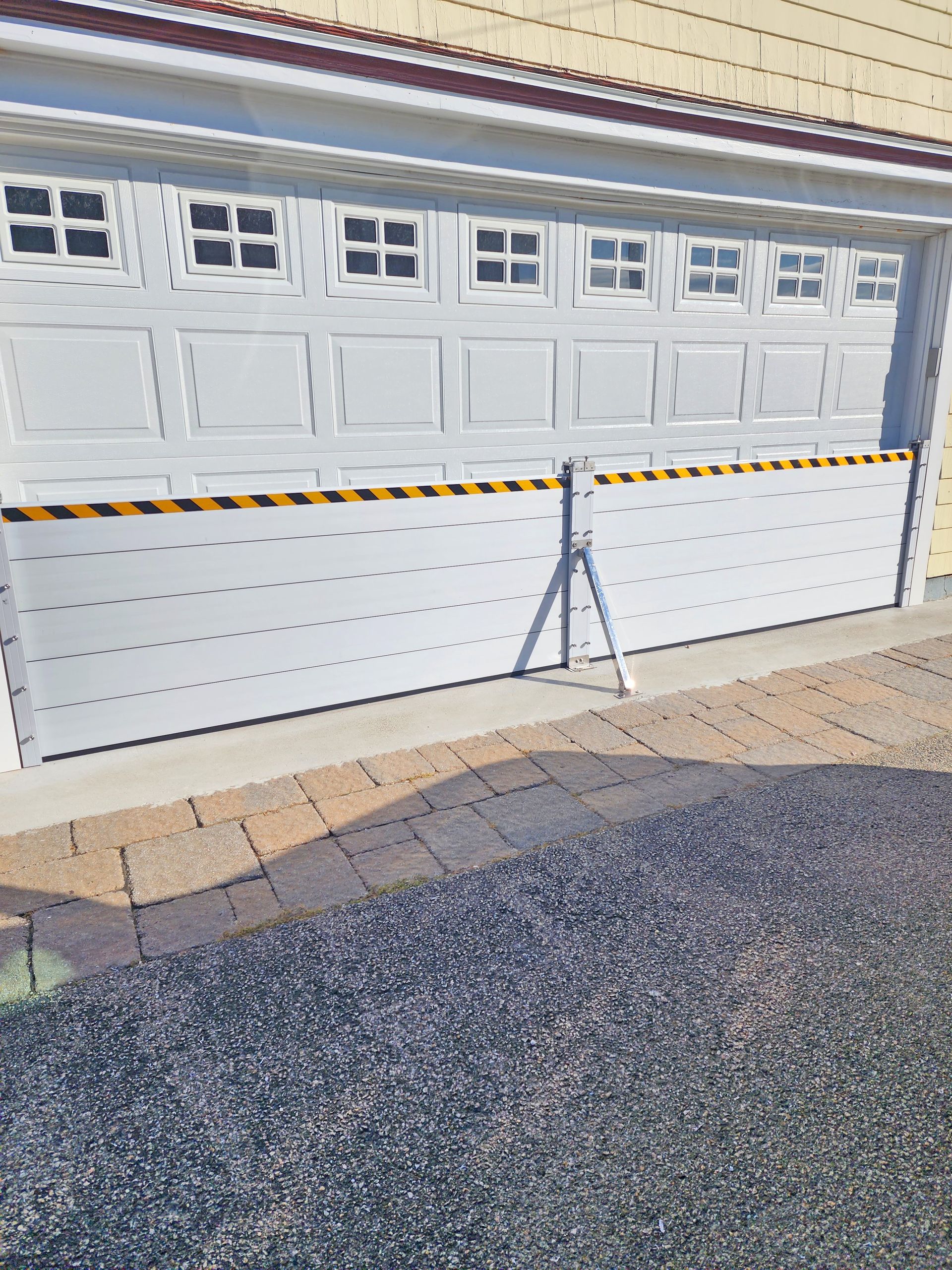White flood barrier in front of a closed garage door, warning stripes at top, tripod support.