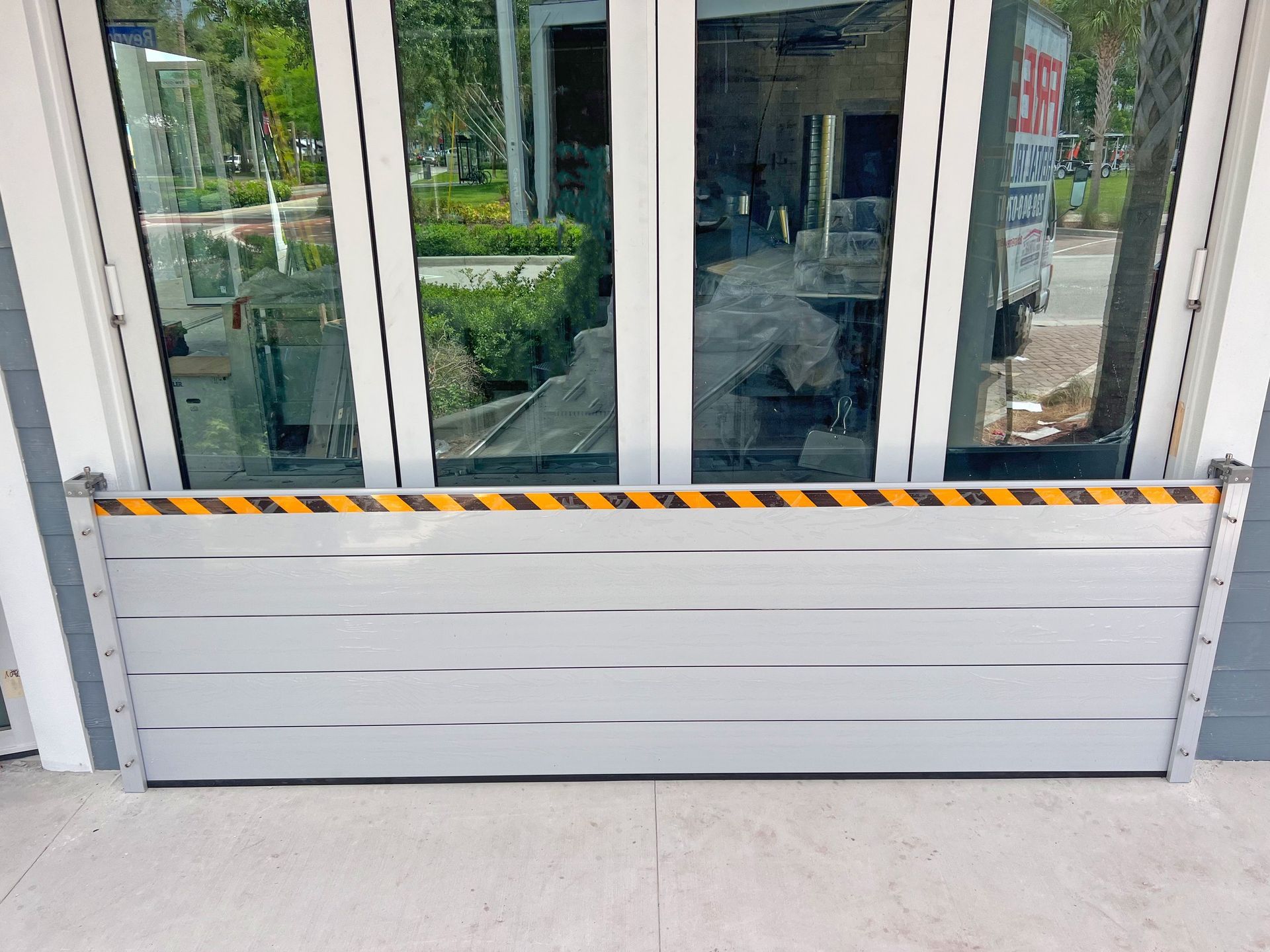 Flood barrier installed in front of glass doors, with yellow and black hazard stripes.